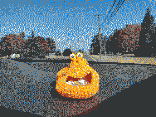 An orange, crocheted object with googly eyes and a hole resembling a smiling mouth is resting on the dashboard of a car