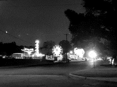 A distant view of a carnival, with the bright and flashy lights from the rides illuminating the dark night sky