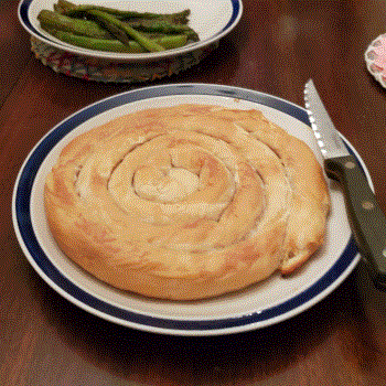 A plate of pastry rolled into a round, spiral shape, by a sideplate of grilled asparagus