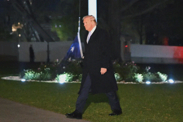 A photo of Donald Trump walking across the lawn of the White House. An American flag has fallen to the ground.