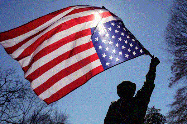 The silhouette of a person waving a large, upside down American flag.