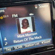 A car radio is playing 'Return of the Mack' by Mark Morrison.